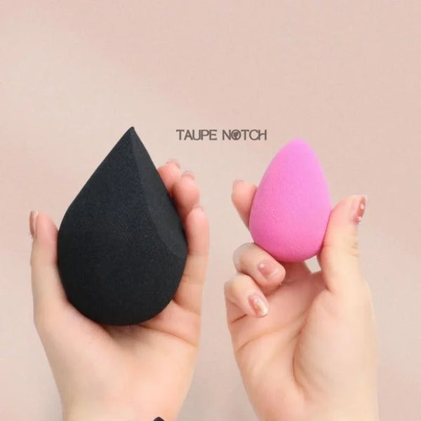 Pair of teardrop beauty sponges: dark gray and pink, held in hands.