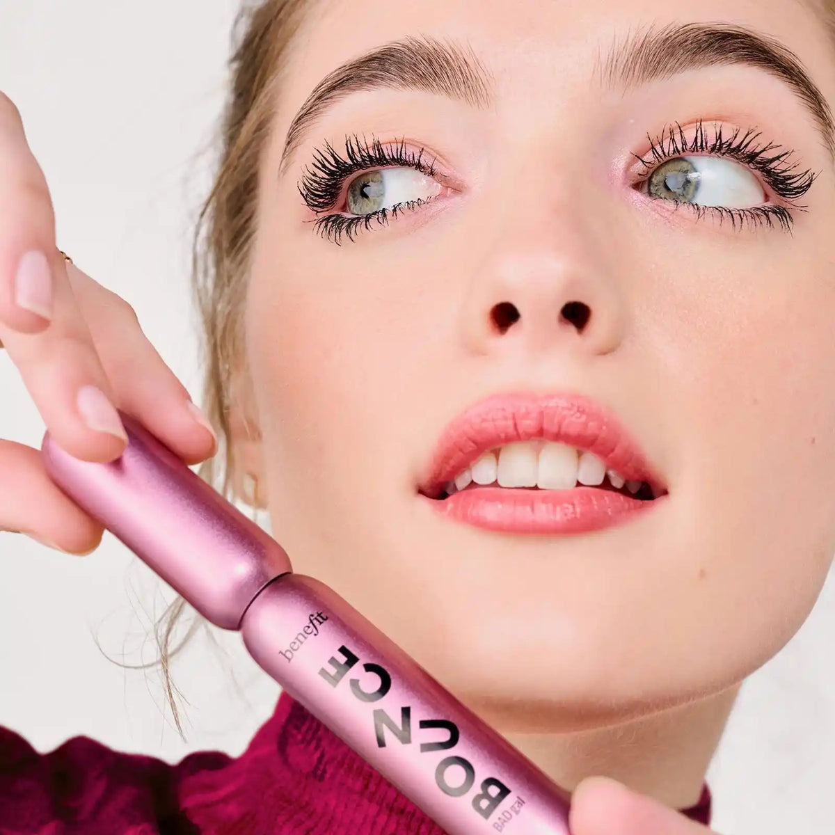 Close-up of a woman holding a Benefit BADGal Bounce Volumizing Mascara with a blurred background