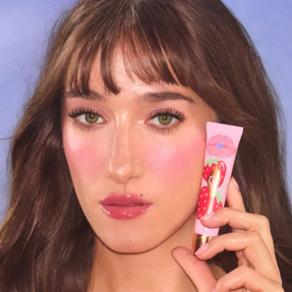 Lip plumper tube held near glossy pink lips in makeup close-up