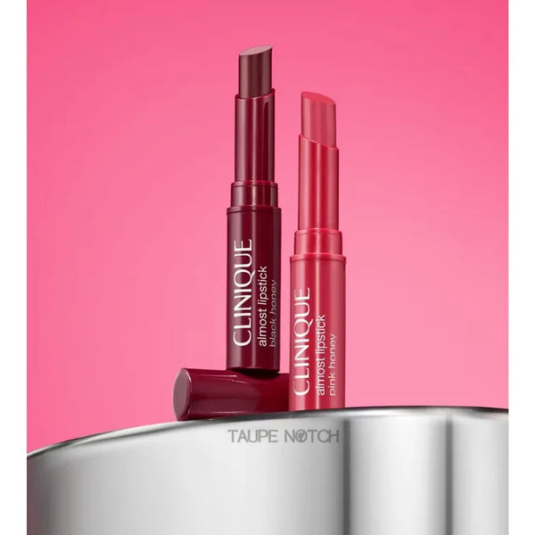Two Clinique lipsticks, one dark berry and one pink, standing on a metal surface