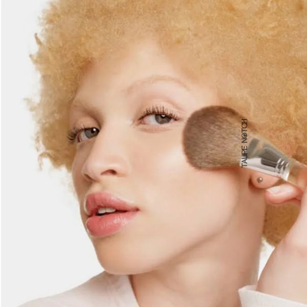 Clinique powder brush held near cheek, rounded dense bristles