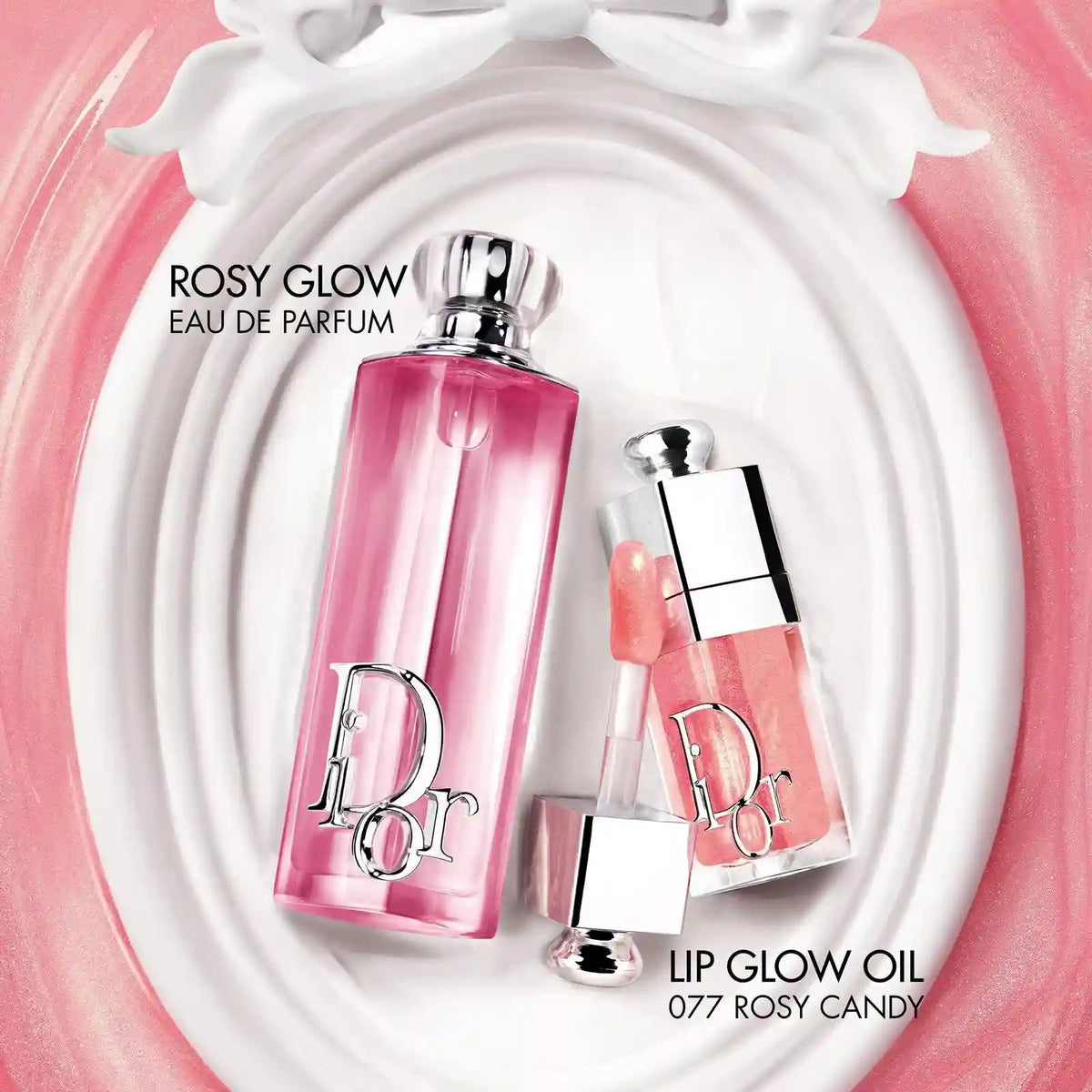 Dior Rosy Glow Eau de Parfum and Lip Glow Oil in shade 077 Rosy Candy, displayed on a white oval dish with pink swirls. The perfume bottle is pink with a silver Dior logo, and the lip oil is a peachy pink with a silver cap.