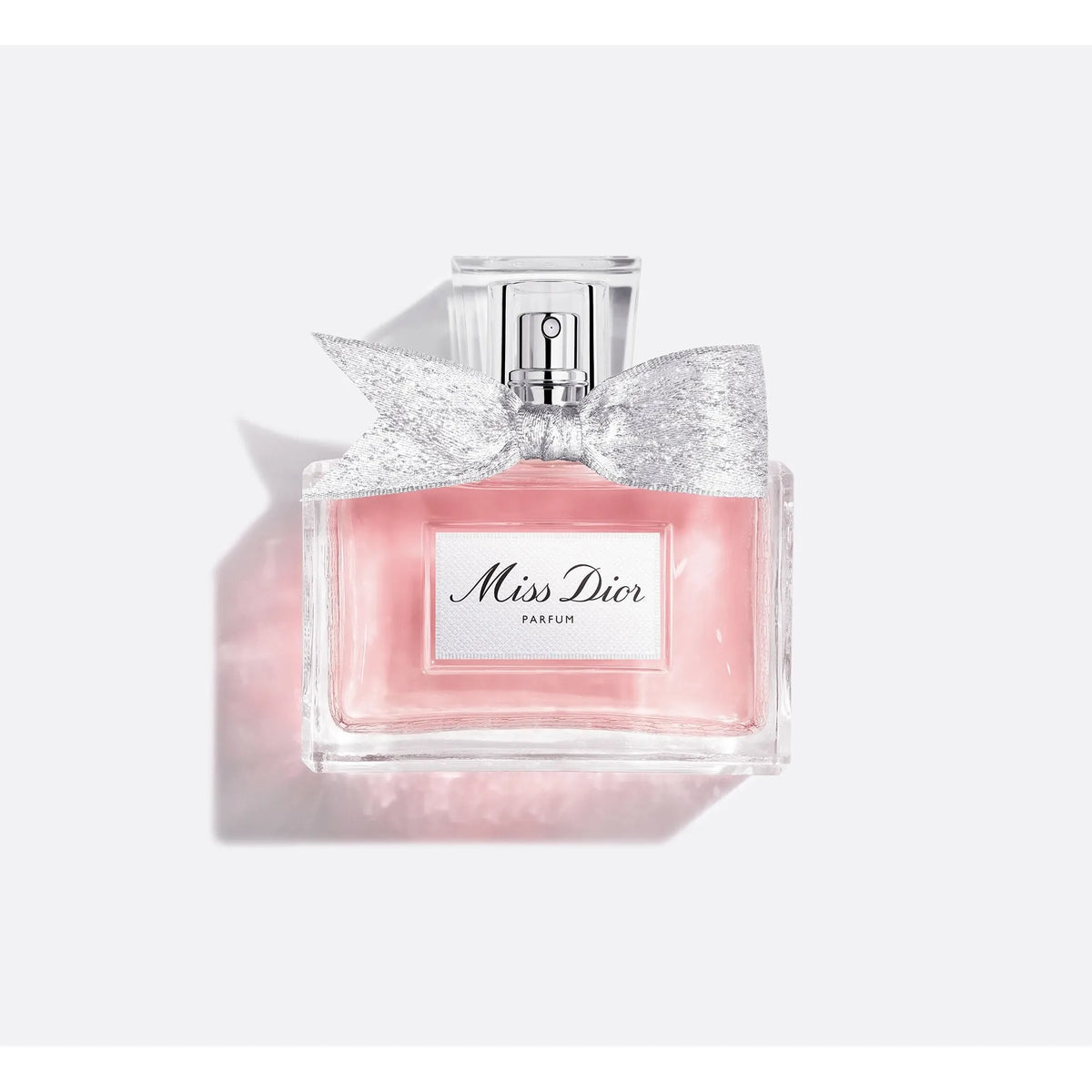 Miss Dior Parfum bottle with a pink liquid, a silver glitter bow, and a silver cap, set against a light gray background with a soft pink shadow.