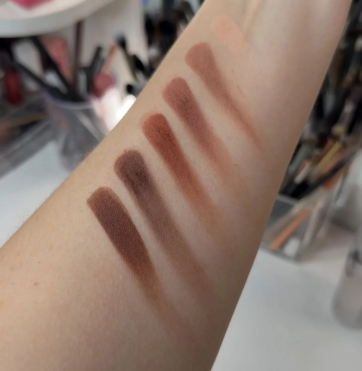 Arm swatches of warm brown and bronze eyeshadows, matte and shimmer tones
