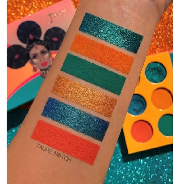 Eyeshadow palette with arm swatches: teal, orange, green, gold, blue, and red shades.