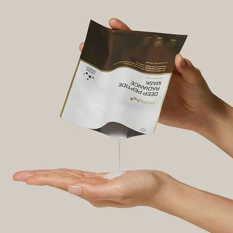 A person holds Medicube Deep Peptide Radiance Mask, with the white mask cream being squeezed onto an open palm against a solid beige background.