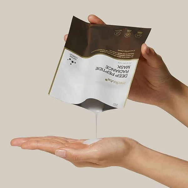 A person holds Medicube Deep Peptide Radiance Mask, with the white mask cream being squeezed onto an open palm against a solid beige background.