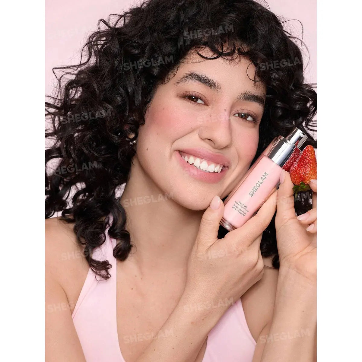 Sheglam face primer bottle held near face, clear cap and pink liquid formula