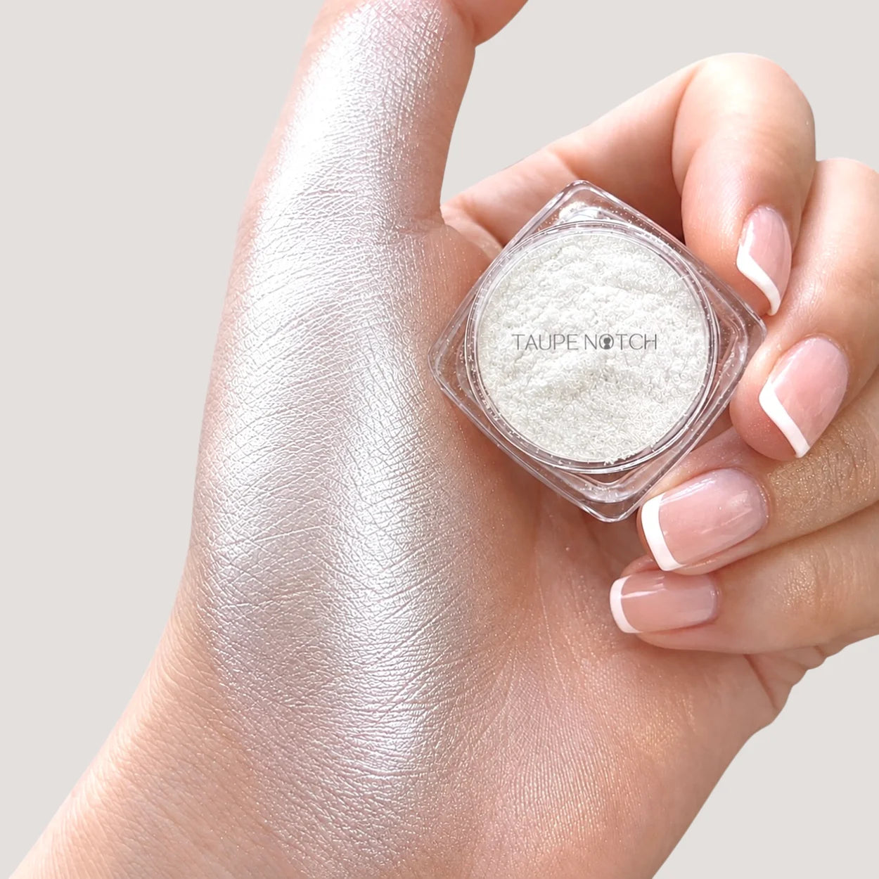Taupe Notch loose highlighter and pigment jar with silver-white powder, held in hand