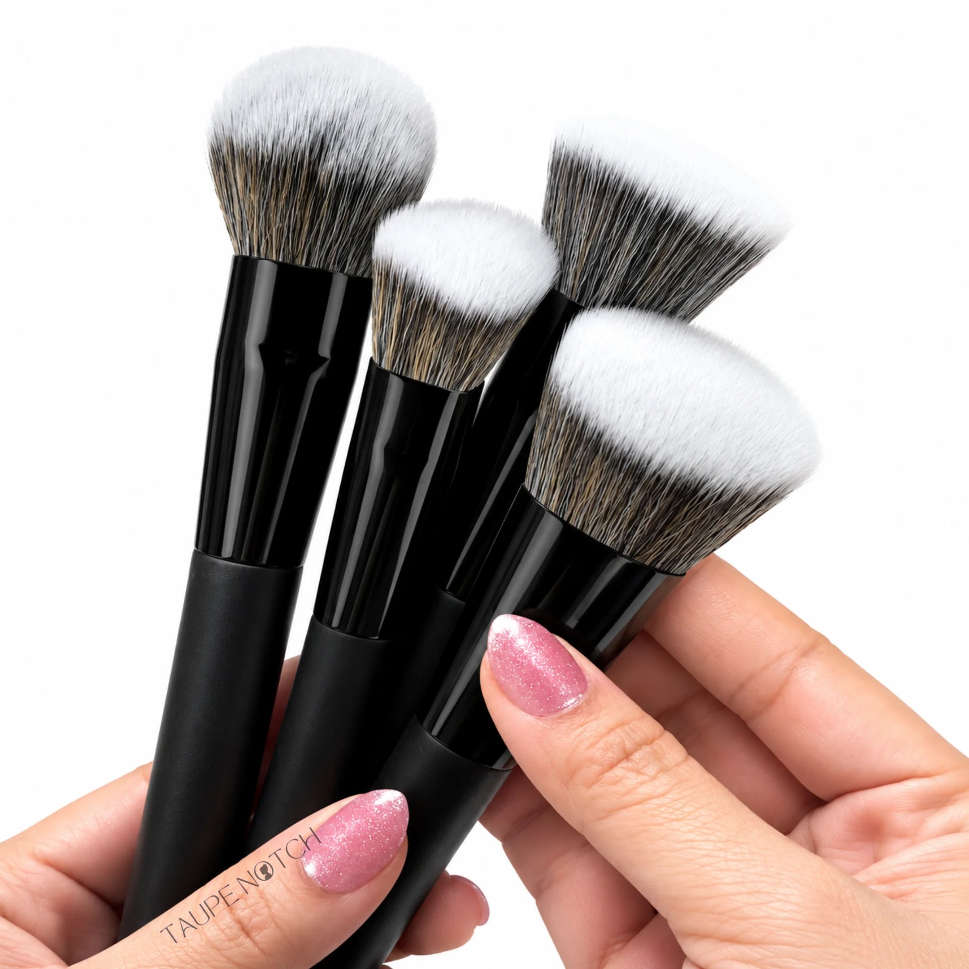 Four-piece makeup brush set with black glossy handles and mixed light-and-dark bristles, held by hand